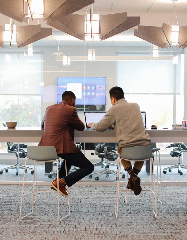 Two First American colleagues sitting at table on laptop with glass walls in front of them.