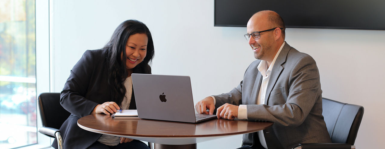 Two First American colleagues sitting at a round table, collaborating on a laptop.