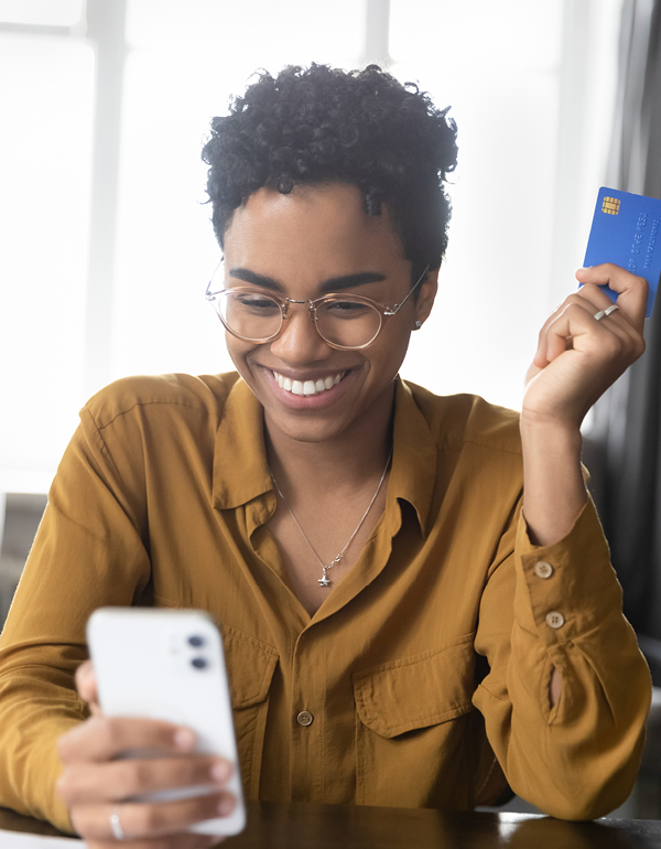 Woman smiling looking at phone and holding credit card.
